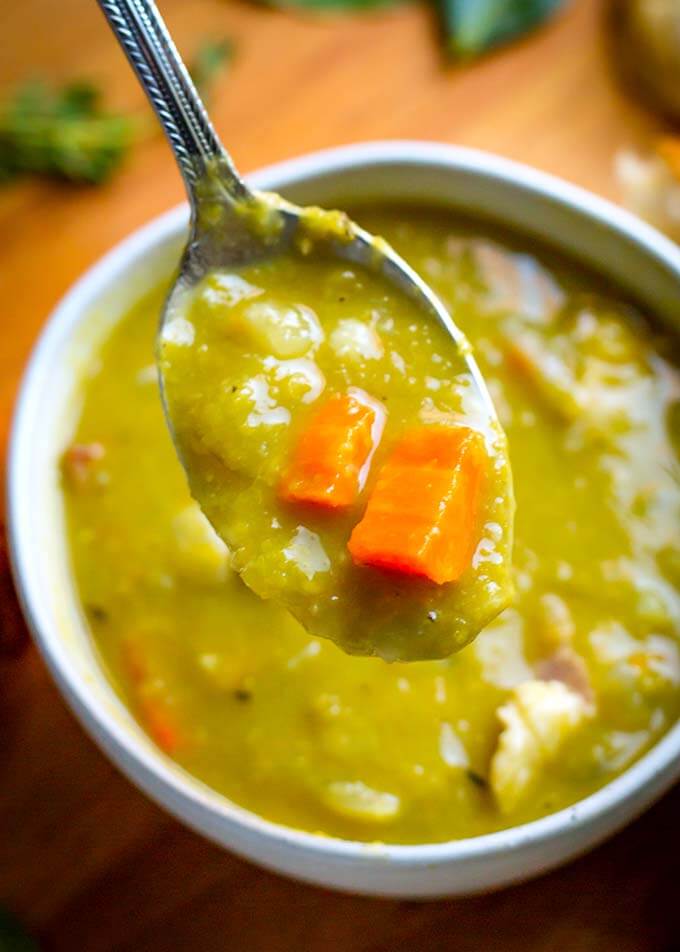 Close up of spoon with Split Pea Soup in a white bowl on wooden background 