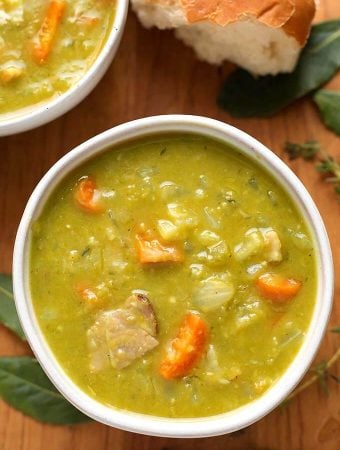 Split Pea Soup in a white bowl on wooden background with broken bread roll