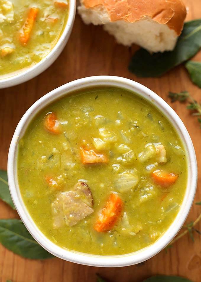 Split Pea Soup in a white bowl on wooden background with broken bread roll 