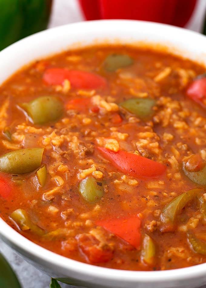 Close up of Stuffed Pepper Soup in white bowl  with green and red bell peppers in background
