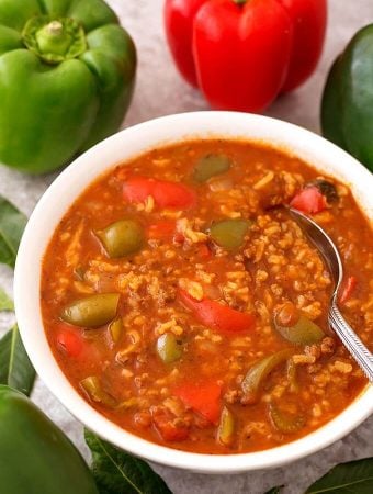 Stuffed Pepper Soup in white bowl with spoon with green and red bell peppers in background