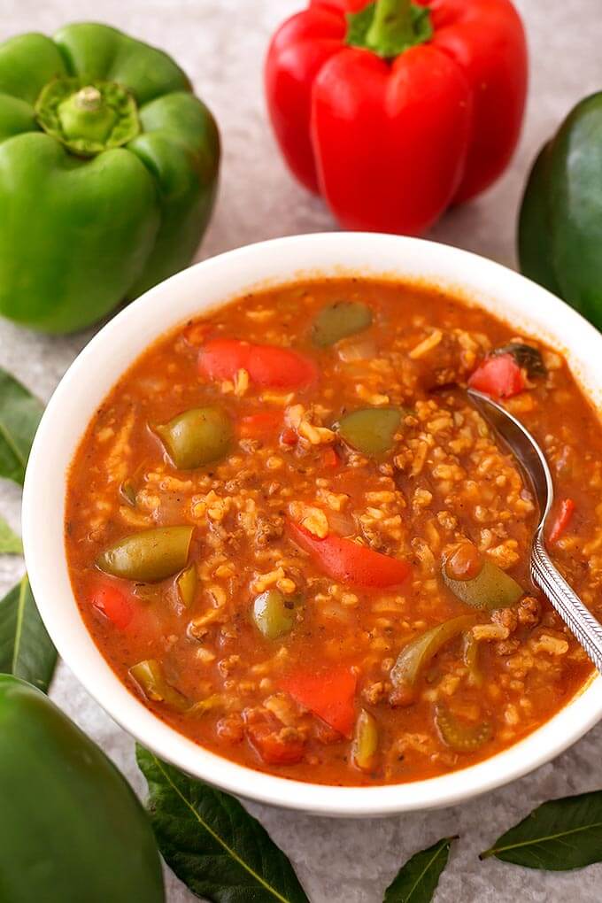 Stuffed Pepper Soup with a spoon in a white bowl surrounded by green peppers and leaves