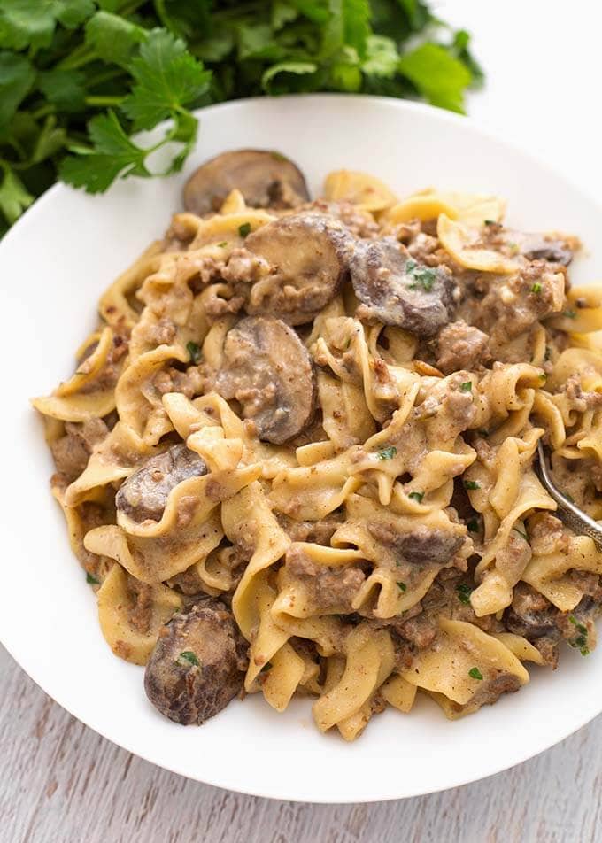 Hamburger Stroganoff on a white plate with fork next to bunch of parsley