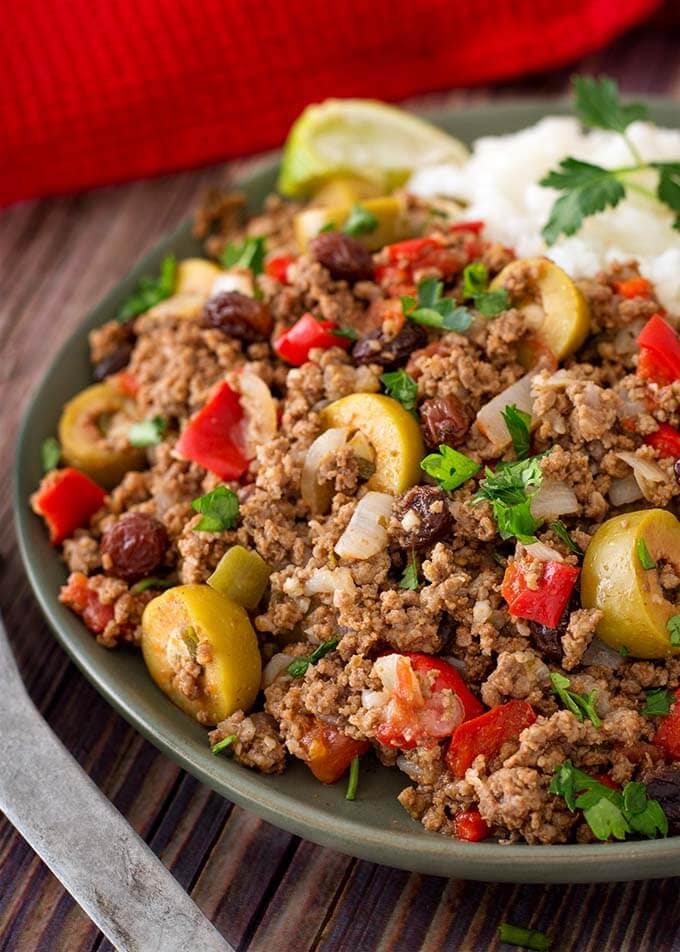 Picadillo with white rice on dark green plate next to silver spoon