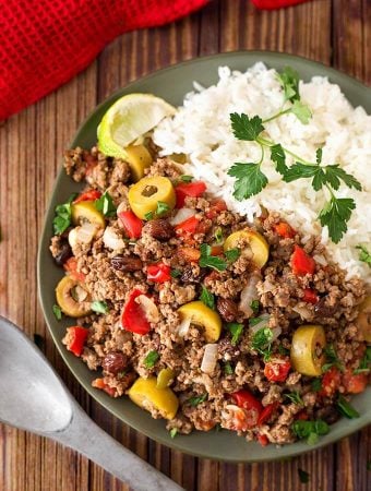 Picadillo with white rice on dark green plate next to silver spoon