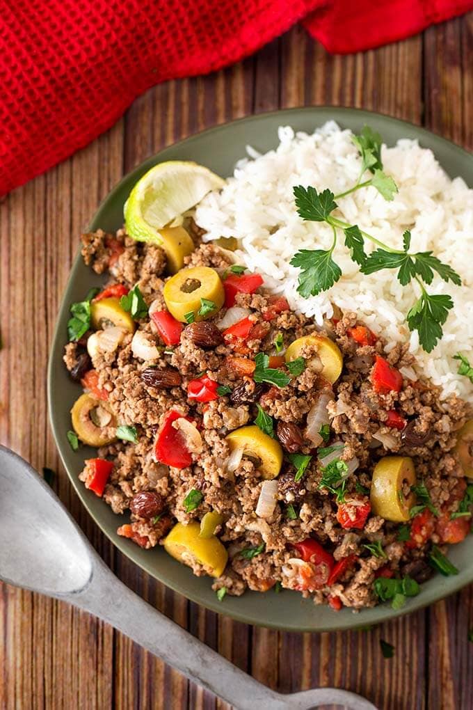 Picadillo with white rice on dark green plate next to silver spoon