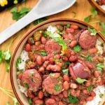 Red Beans and Rice in beige bowl next to serving spoon all on wooden board