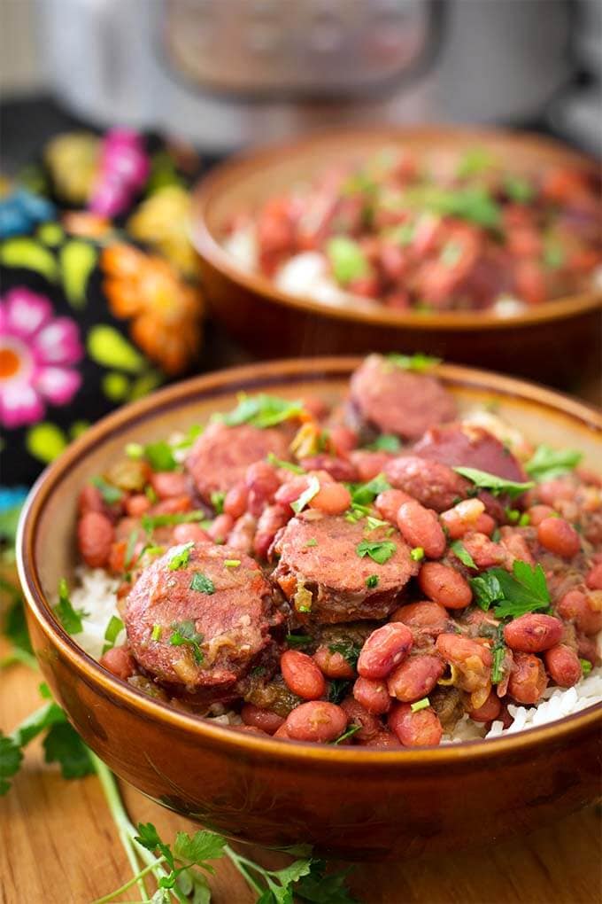 Two brown bowls of Red Beans and Rice With Sausage on wooden board in front of pressure cooker