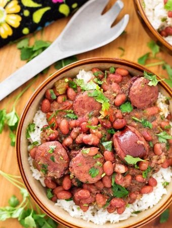 Red Beans and Rice in beige bowl next to serving spoon all on wooden board