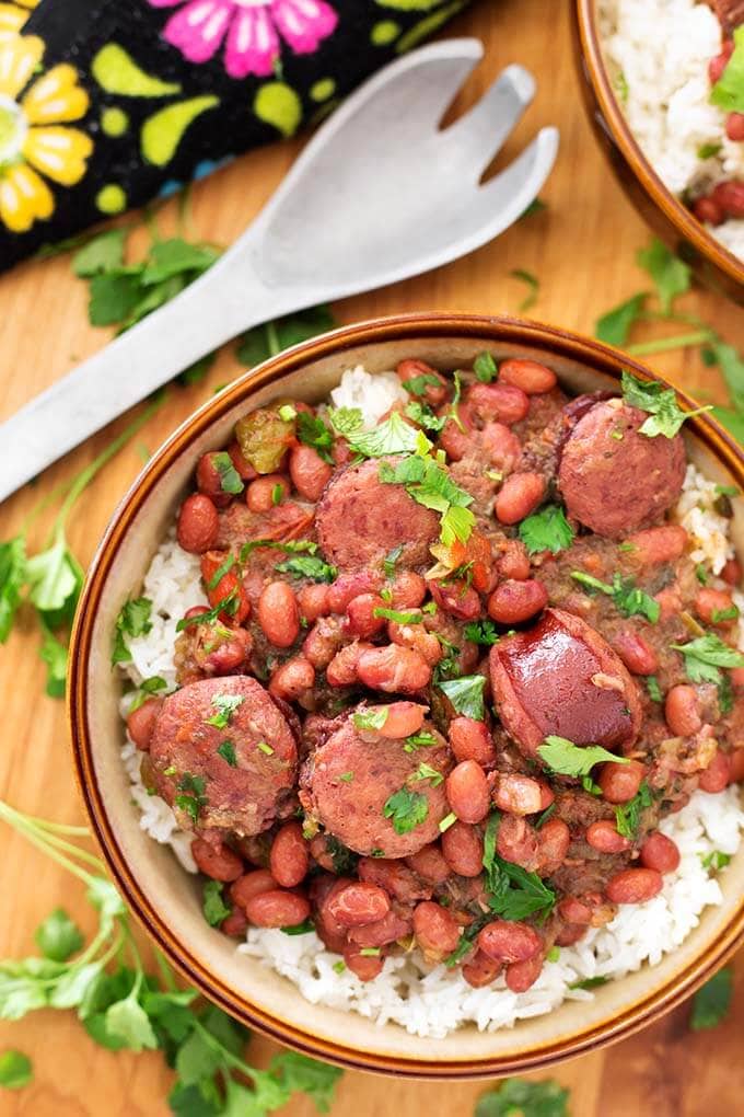 Red Beans and Rice in beige bowl next to serving spoon all on wooden board