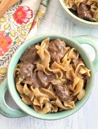 Beef and Noodles in turquoise bowl with handles on light wood background