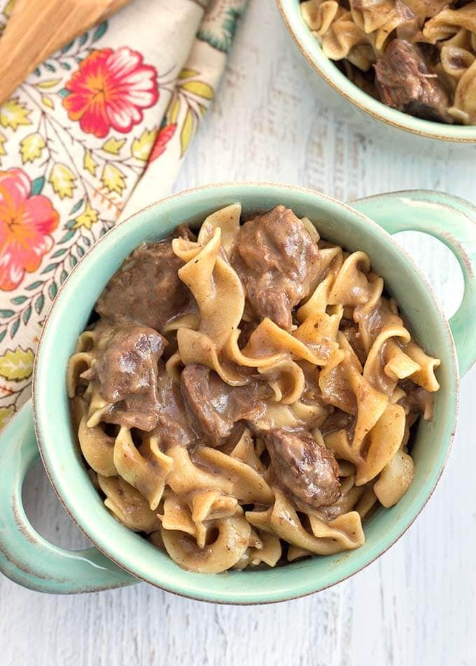 Beef and Noodles in turquoise bowl with handles on light wood background