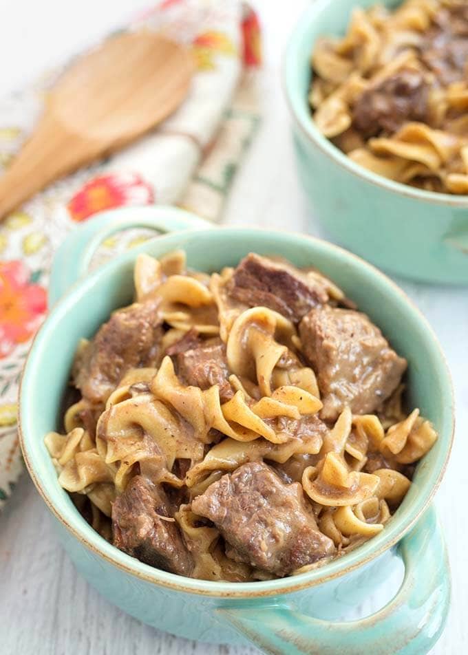 Beef and Noodles in turquoise bowl with handles on light wood background