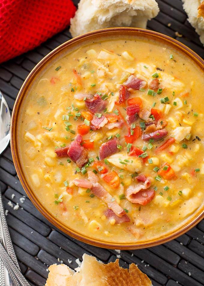 Chicken Corn Chowder in a brown bowl next to spoon and bread chunks