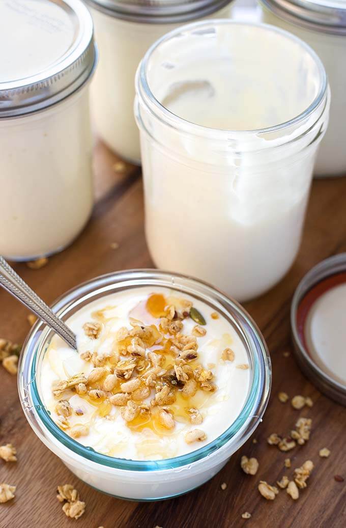 small glass bowl of yogurt next to glass jars with yogurt