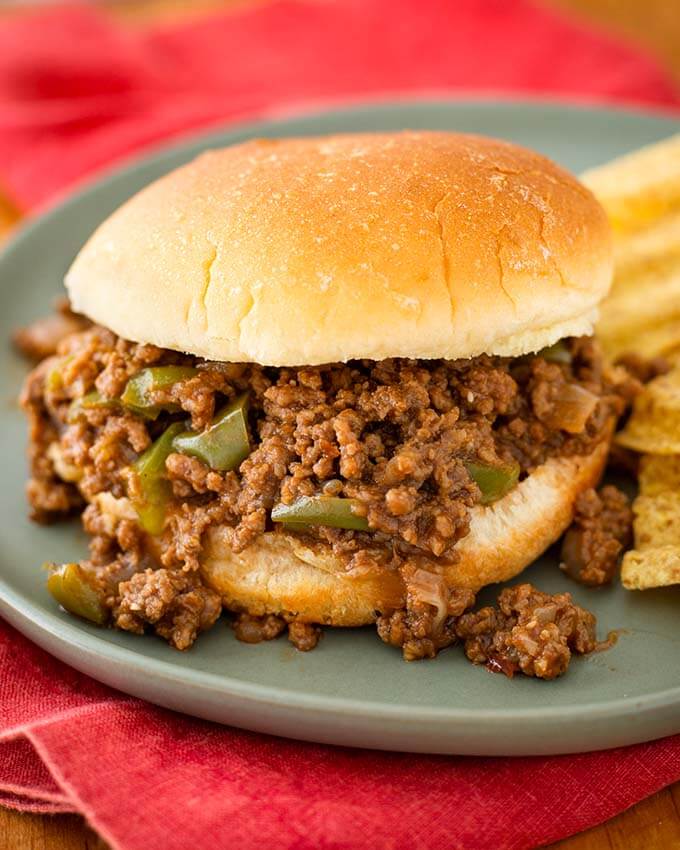 Sloppy Joes on hamburger bun next to chips all on blue plate