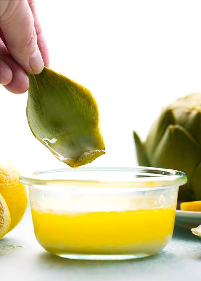 hand dipping part of artichoke into a small bowl of melted butter