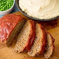 Instant Pot Sliced Meatloaf on a wooden cutting board and Mashed Potatoes in a black bowl