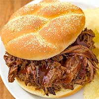 Instant Pot Barbecue Beef on a hamburger bun next to potato chips all on a white plate