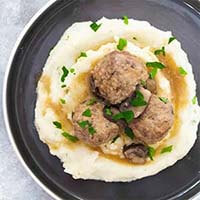 Instant Pot Salisbury Steak Meatballs over mashed potatoes on a black plate