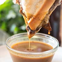 Hand dipping Instant Pot French Dip Sandwiches in juice