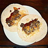 Two Instant Pot Beef Carnitas on tortillas and a white plate