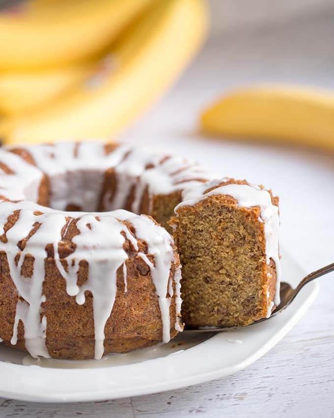 Banana Bread with vanilla icing glaze on a white plater with a slice being served with  silver spoon