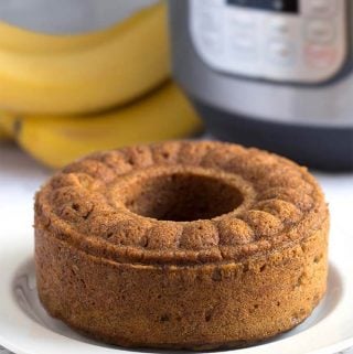 Bunt loaf of Banana Bread on a white plate in front of a pressure cooker