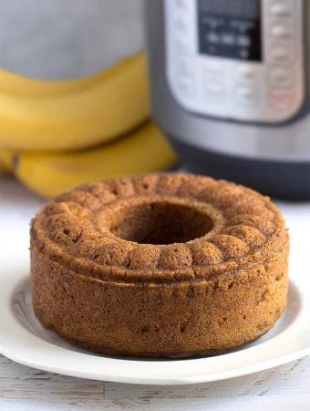 Bunt loaf of Banana Bread on a white plate in front of a pressure cooker