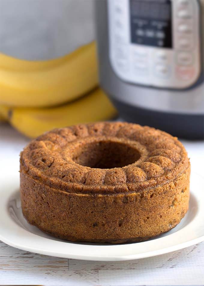 Bunt loaf of Banana Bread on a white plate in front of a pressure cooker