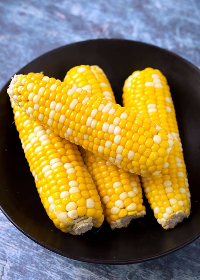 Four Corn on the Cobs on a black plate