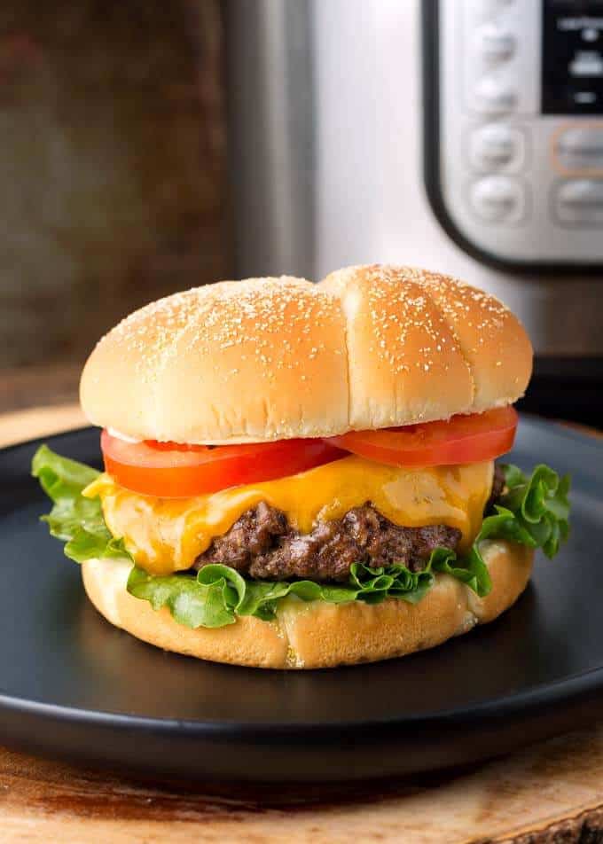 Hamburgers with cheese, lettuce, and tomato on a black plate in front of a presure cooker