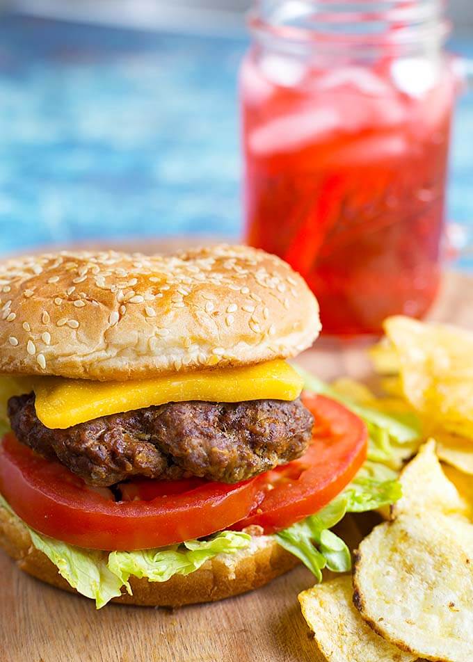 Hamburgers next to potato chips on a wooden board