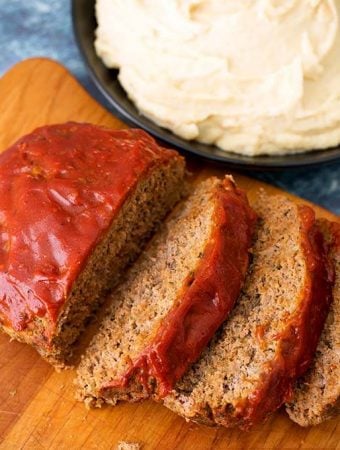 Sliced Meatloaf on a wooden cutting board with a black bowl full Mashed Potatoes