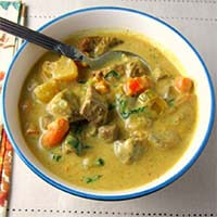 Instant Pot Beef Curry in a white bowl with blue rim and a silver spoon