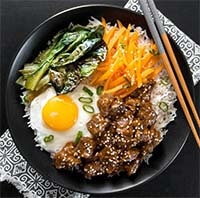 instant pot korean beef with cooked egg and vegetables over rice in a black bowl with chopsticks