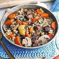 Instant Pot Beef Barley Mushroom Soup in a gray bowl on a blue place mat