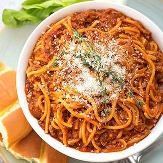 Spaghetti in a white bowl next to bread