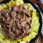 Kalua Pork on top of cooked cabbage on a black plate