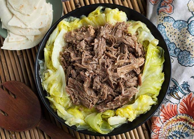 Top view of Kalua Pork on cooked cabbage on a black plate