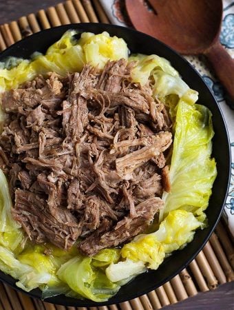 Kalua Pork on top of cooked cabbage on a black plate