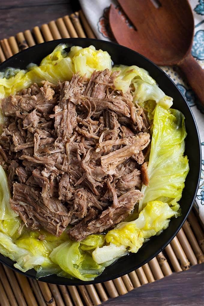 Kalua Pork on top of cooked cabbage on a black plate