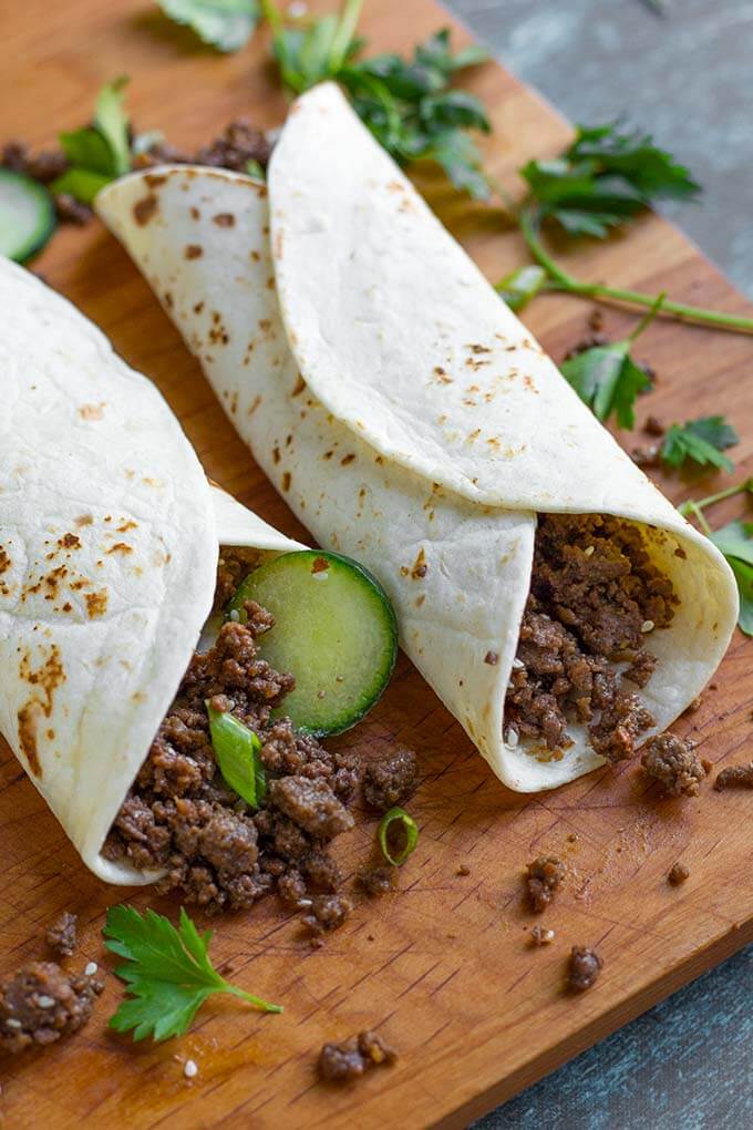 Korean Ground Beef rolled in flour tortillas on a wooden board