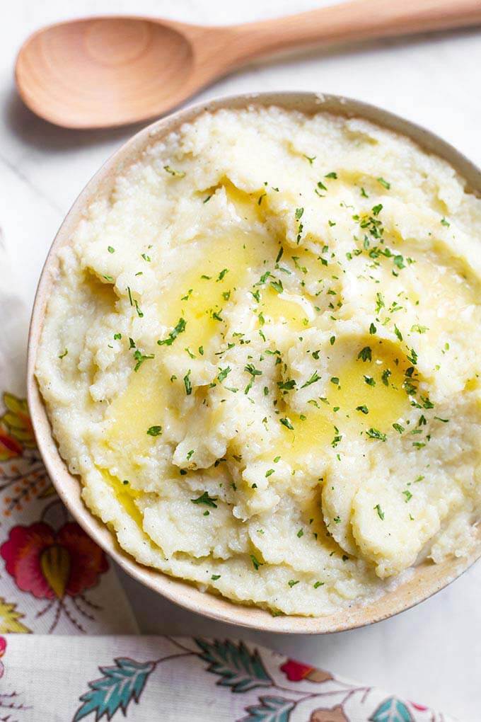 Mashed Cauliflower in a beige bowl next to a wooden spoon