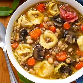 Tortellini Soup in a white bowl next to a silver spoon