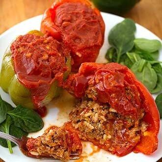 Three Stuffed Peppers on a white plate with baby leafed spinach