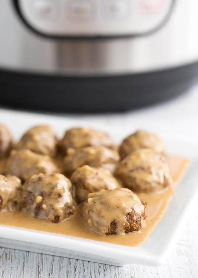 Swedish Meatballs on a white plate in front of a pressure cooker
