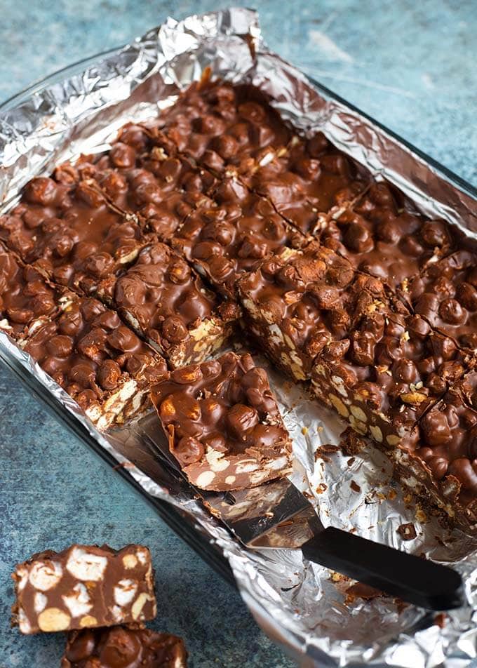 Foil-lined baking pan of 5 Ingredient Chocolate Peanut Bars with one being served with a silver spatula