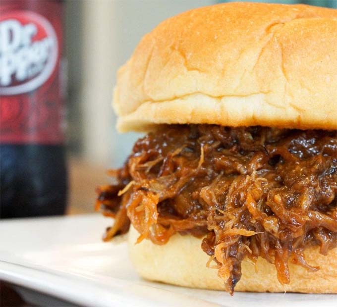 Dr Pepper pulled pork on a hamburger bun on a white plate