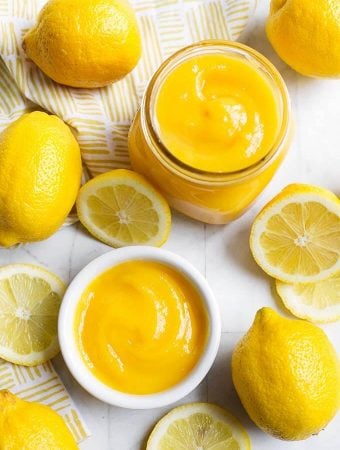 Lemon Curd in a small glass jar and white bowl, all surrounded by cut lemons